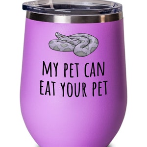 Puede incluir: Un vaso de vino aislado de color lavanda con borde y tapa plateados. El vaso presenta una ilustración de dibujos animados de una serpiente gris y el texto "MY PET CAN EAT YOUR PET" en negro.