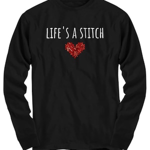 May include: Black long-sleeved shirt with the text "Life's a Stitch" in white and a red embroidered heart.