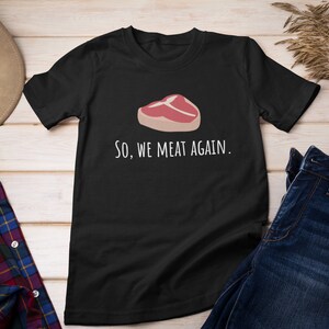 May include: Black t-shirt with a white graphic of a steak and the text "So, we meat again."