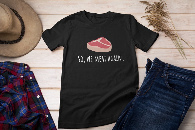 May include: Black t-shirt with a white graphic of a steak and the text "So, we meat again."