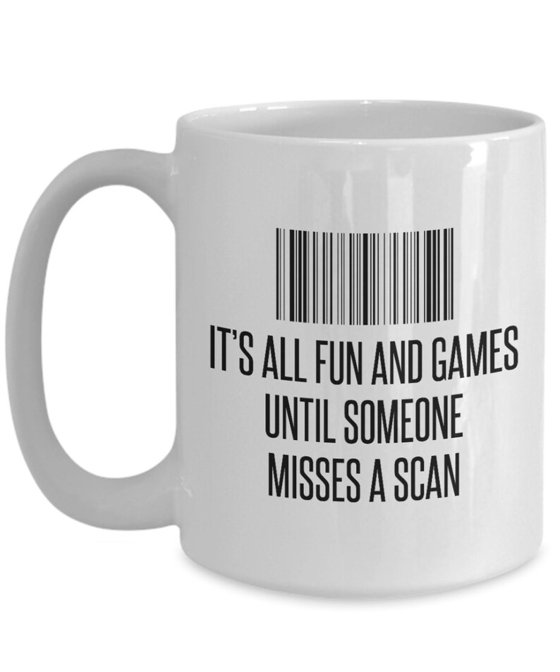 May include: White ceramic mug with a black barcode graphic and the text "IT'S ALL FUN AND GAMES UNTIL SOMEONE MISSES A SCAN". The mug has a curved handle and a cylindrical shape.