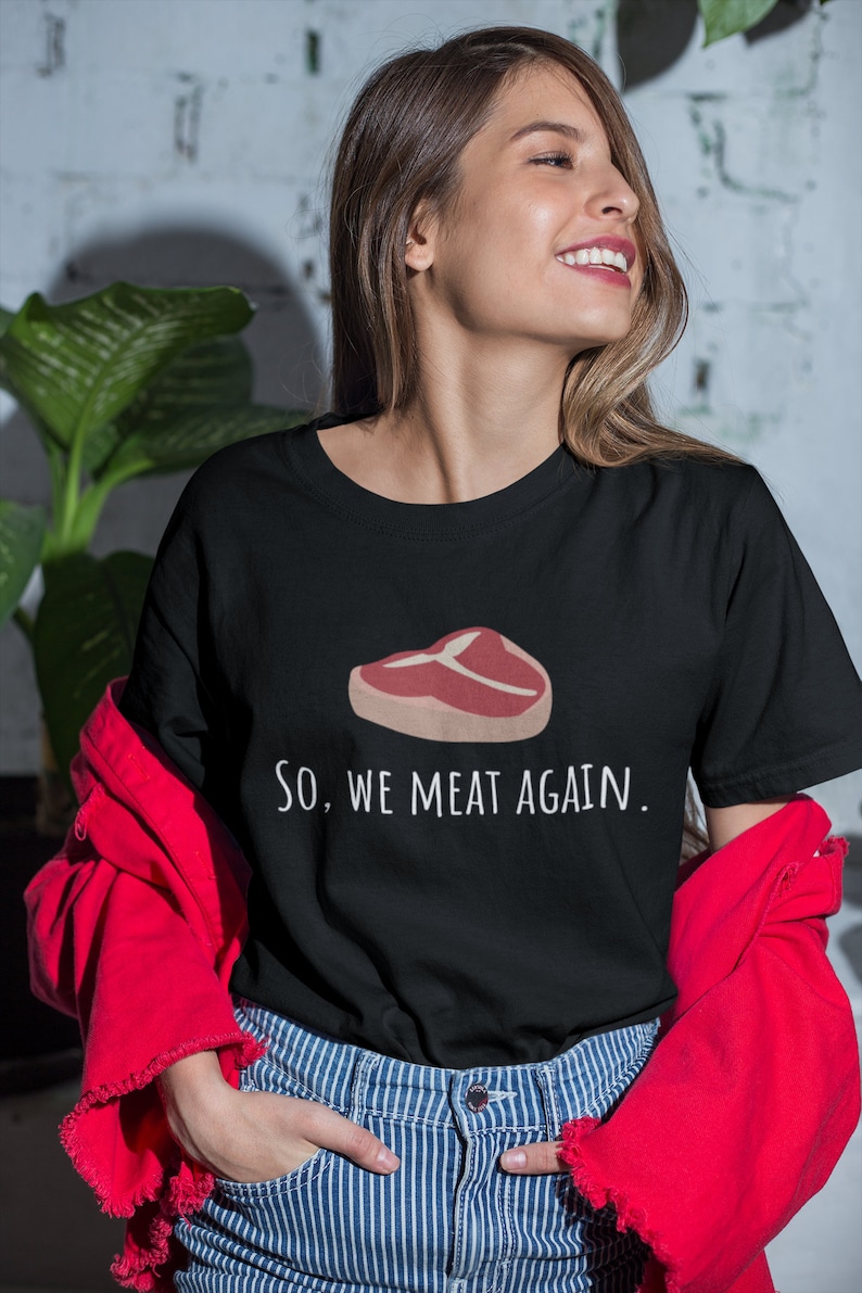 May include: A black t-shirt with a white graphic of a steak and the text "So, we meat again."