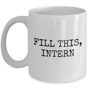 May include: White ceramic mug with a curved handle. The mug features the text "FILL THIS, INTERN" in black, bold, typewriter-style font. A humorous office gift.