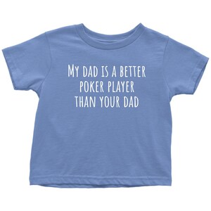 May include: A light blue toddler t-shirt with the text "My Dad is a Better Poker Player Than Your Dad" printed in white.
