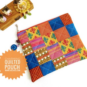 K&ouml;nnte beinhalten: Eine farbenfrohe gesteppte Tasche mit Rei&szlig;verschluss. Die Tasche besteht aus Patchwork-Stoff in den Farben Blau, Orange, Gelb, Rosa und Gr&uuml;n. Die Tasche hat einen Anh&auml;nger an der Rei&szlig;verschlusslasche.