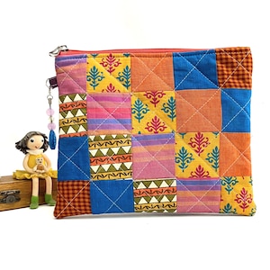 K&ouml;nnte beinhalten: Eine farbenfrohe Patchwork-Tasche mit Rei&szlig;verschluss aus Stoff mit verschiedenen Mustern in Orange-, Gelb-, Blau-, Rosa- und Gr&uuml;nt&ouml;nen. Die Tasche hat einen Rei&szlig;verschluss und einen Perlenanh&auml;nger.
