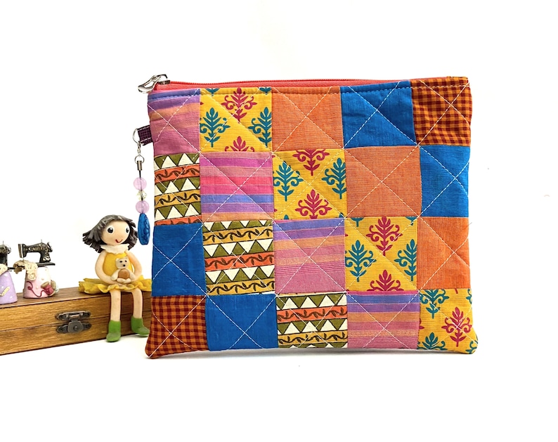K&ouml;nnte beinhalten: Eine farbenfrohe Patchwork-Tasche mit Rei&szlig;verschluss aus Stoff mit verschiedenen Mustern in Orange-, Gelb-, Blau-, Rosa- und Gr&uuml;nt&ouml;nen. Die Tasche hat einen Rei&szlig;verschluss und einen Perlenanh&auml;nger.