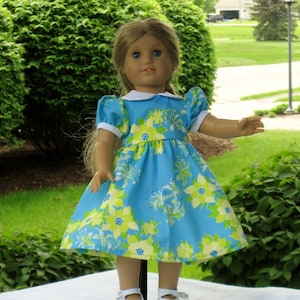 Könnte beinhalten: Eine Puppe in einem blauen und gelben Blumenkleid mit weißem Kragen und weißen Schuhen.