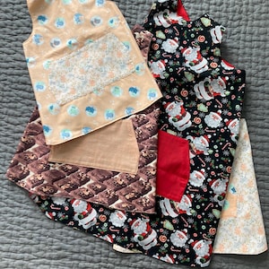 May include: Four sleeveless aprons with different patterns. One is peach with a floral pocket, one is brown with a brick pattern, one is black with a Santa Claus pattern, and one is white with a floral pattern.