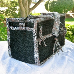 May include: A black and white patterned tote bag with a zipper closure and a long strap. The bag has a variety of pockets and compartments.