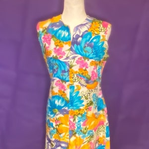 May include: A sleeveless maxi dress with a white background and a colorful floral print. The flowers are in shades of blue, yellow, pink, and orange.