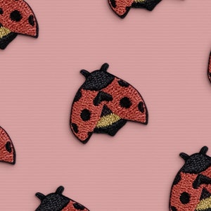 May include: A collection of red and black ladybug patches on a pink background. The ladybugs have black spots and gold accents.