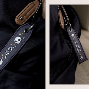 May include: A black backpack with two zippered pouches and a black and white embroidered keychain that says "Til Death Do Us Part" with a skull and crossbones design.