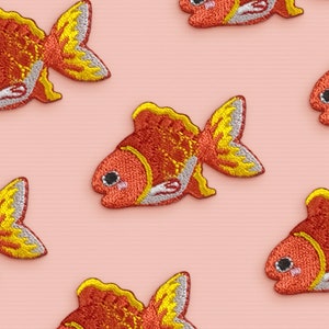 May include: Six embroidered gold fish patches on a pink background. The fish are orange and yellow with white accents.