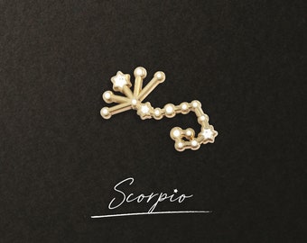 Puede incluir: Encanto de constelación de Escorpio en tono dorado con estrellas de esmalte blanco. El encanto está sobre un fondo negro y la palabra "Escorpio" está escrita en cursiva debajo del encanto.