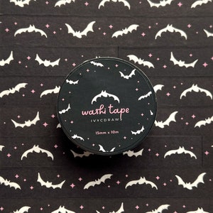 Könnte beinhalten: Eine Rolle schwarzes Washi-Tape mit einem Muster aus weißen Fledermäusen und rosa Sternen. Das Band ist 15 mm breit und 10 m lang. Das Etikett auf dem Band lautet "washi tape IVYCDRAWS 15mm x 10m".