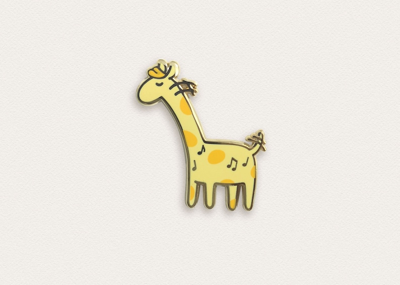 May include: A gold-colored enamel pin featuring a cartoon giraffe with yellow spots and musical notes. The giraffe has a closed eye and a small flower on its head.