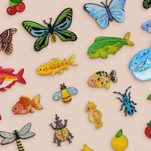 May include: A collection of colourful embroidered iron-on patches featuring various designs, including butterflies, fish, a ladybug, a dragonfly, a bee, a seahorse, a shark, a pufferfish, and a beetle.