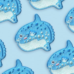 May include: Six blue and white embroidered patches of a cartoon mola mola fish. The fish have a white belly and blue spots. The fish have a pink mouth and a white fin.