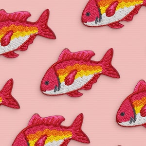 May include: Six embroidered red and orange fish patches on a pink background. The fish have white bellies and black eyes.