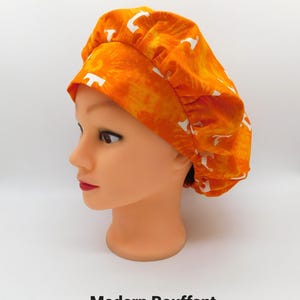 May include: An orange bouffant cap with a white pattern is displayed on a mannequin head. The cap has a tie-dye effect and is gathered at the back. The text "Modern Bouffant" is at the bottom of the image.