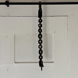 May include: A black metal adjustable hanging chain featuring a series of circular cutouts along its length. The chain is suspended from a horizontal black rod and terminates in a small hook at the bottom, designed for vertical length adjustment.