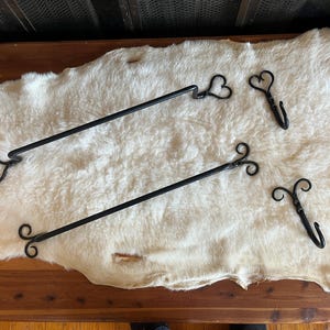 Puede incluir: Herramientas de chimenea de hierro forjado negro, que incluyen dos atizadores con diseños en forma de corazón y volutas, y dos ganchos. Las herramientas se exhiben sobre una alfombra de piel de oveja blanca, con una superficie de madera debajo.