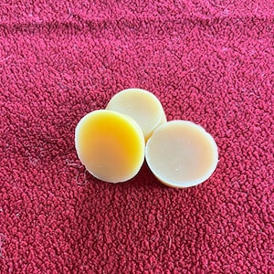 Puede incluir: Tres discos redondos de cera de color amarillo sobre una superficie roja y peluda.