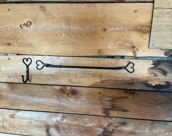 May include: A black metal wall hook and a matching black metal towel bar, both featuring decorative heart-shaped ends. The hook has a single curved arm, while the horizontal bar is straight with a heart design at each end for mounting.
