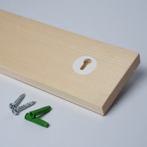 K&ouml;nnte beinhalten: Ein Holzregal mit einer wei&szlig;en Kunststoff-Schl&uuml;sselloch-Abdeckung und zwei Schrauben und Kunststoffd&uuml;beln zur Montage.