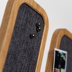 Könnte beinhalten: Nahaufnahme von zwei Holzrahmen-Memoboards. Die Boards haben eine graue Stoffmitte und sind mit einem hellbraunen Holzrahmen akzentuiert. Drei silberne magnetische Kugelstifte sind am Stoff befestigt. Ein Foto ist am zweiten Board befestigt.