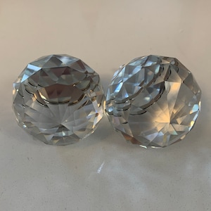 Puede incluir: Dos candelabros de cristal transparente facetado. Los soportes esféricos tienen un diseño geométrico y reflejan la luz, creando un efecto brillante. Los candelabros son redondos y tienen una pequeña abertura en la parte superior para velas.