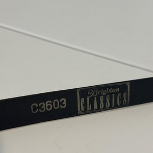 May include: Close-up of a black leather belt with the text "C3603" and "Brighton CLASSICS" in silver lettering. The belt is on a white surface.