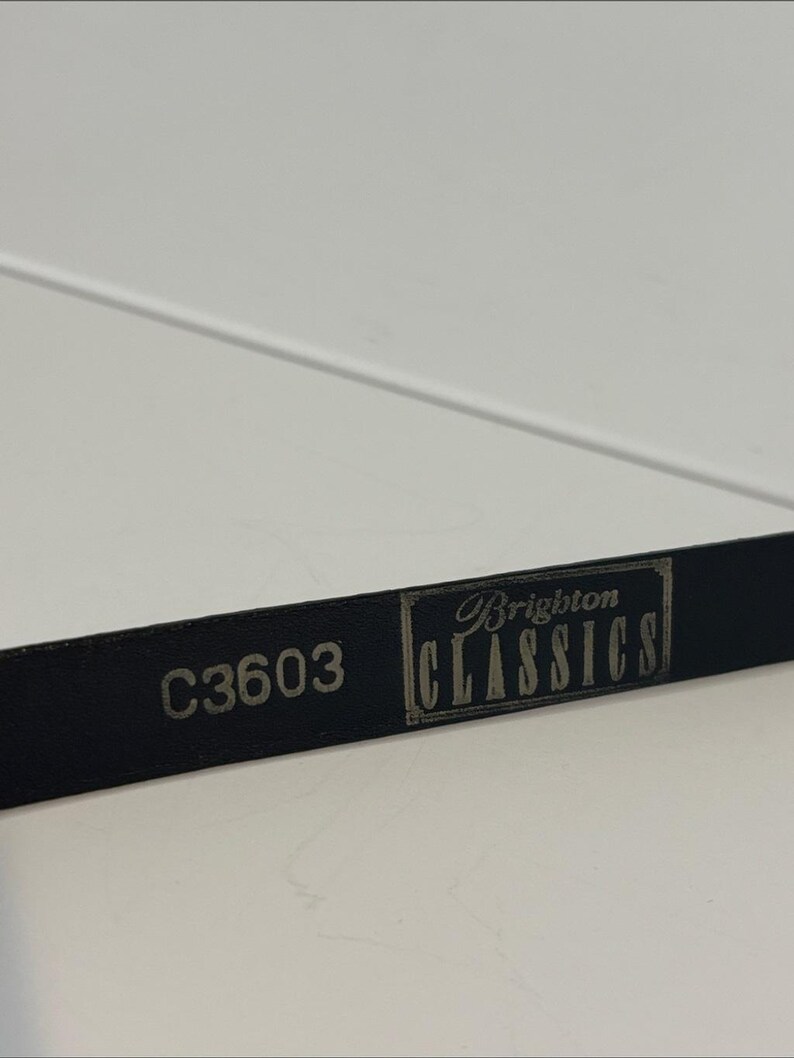 May include: Close-up of a black leather belt with the text "C3603" and "Brighton CLASSICS" in silver lettering. The belt is on a white surface.