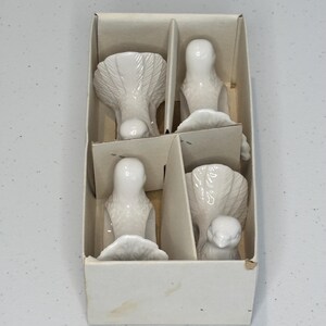 Peut inclure: Un ensemble de six figurines d'oiseaux en porcelaine blanche dans une boîte en carton divisée. Les oiseaux sont dans diverses poses, dont debout et avec les ailes déployées. La boîte est simple et de conception épurée.
