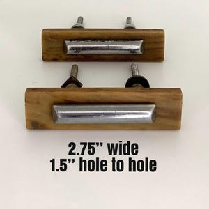 Puede incluir: Dos tiradores de armario de madera con forma rectangular y un acento de metal plateado. Los tiradores miden 7 cm de ancho y tienen una distancia de agujero a agujero de 3,8 cm. Cada tirador tiene dos tornillos para el montaje.