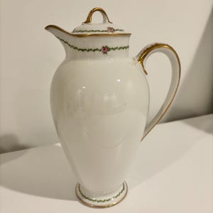 May include: A white porcelain coffee pot with a lid, handle, and spout. The pot is decorated with gold trim and a green and pink floral pattern. The pot is approximately 25 cm tall.