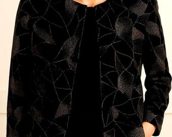 May include: Black open-front jacket with a geometric pattern. The jacket features a textured design with silver stitching outlining the shapes. The jacket is worn over a black top, creating a layered look. The jacket has long sleeves.