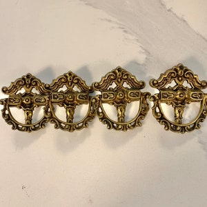 Peut inclure: Quatre poignées de tiroir antiques en laiton avec des motifs symétriques ornés. Chaque poignée présente un dessus décoratif, une poignée centrale et une base incurvée. Le laiton a une patine chaude et vieillie, suggérant une quincaillerie vintage ou d'inspiration vintage.