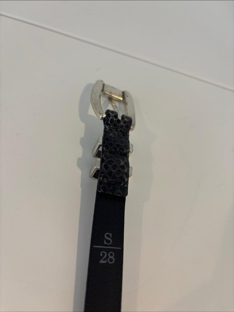May include: Black belt with a silver buckle and a textured snakeskin pattern. The belt is labeled with the size "S" and the number "28".