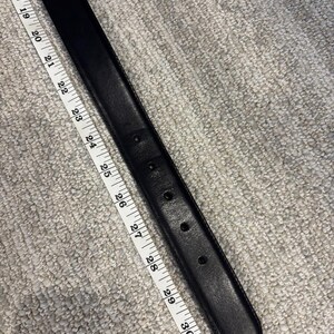 May include: A black belt with a series of adjustment holes, positioned alongside a white measuring tape that indicates a length measurement extending from 17 inches to 31 inches along the strap of the belt.