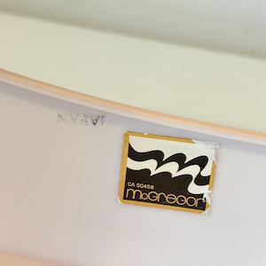 May include: A close-up of a white surface with a gold-edged label. The label features a black and white wavy design and the name "McGregor" in a stylized font. The word "JAPAN" is printed on the surface.