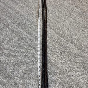 May include: Two dark brown leather belts with silver buckles, each approximately 33 inches long, are laid side by side. The belts have a woven texture and are positioned vertically against a gray textured background.