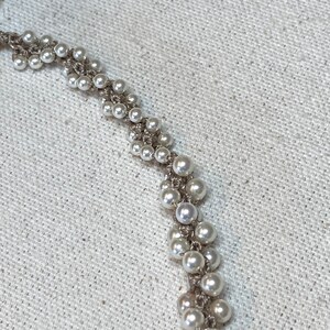 May include: A close-up of a white pearl necklace with a delicate chain design. The necklace is made of small, round pearls that are strung together in a repeating pattern.