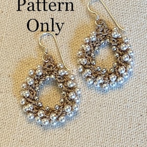 May include: A pair of crocheted earrings with white beads and a silver hook. The earrings are circular in shape and have a delicate, feminine design.