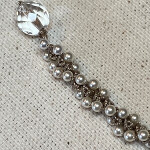 May include: A delicate bracelet with a clear crystal charm and white pearl beads strung on a silver chain.