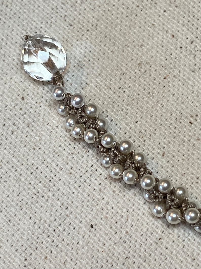 May include: A delicate bracelet with a clear crystal charm and white pearl beads strung on a silver chain.