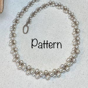 Può includere: Una collana di perle bianche con una chiusura argentata. La collana è composta da due fili di perle, con le perle disposte in un motivo di file alternate.