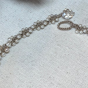 May include: A white pearl and crocheted bracelet with a clear crystal charm.