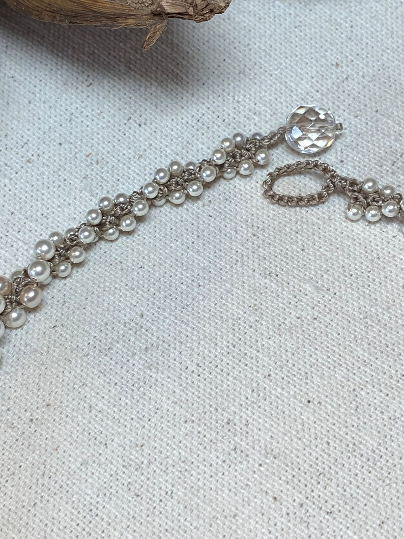 May include: A white pearl and crocheted bracelet with a clear crystal charm.